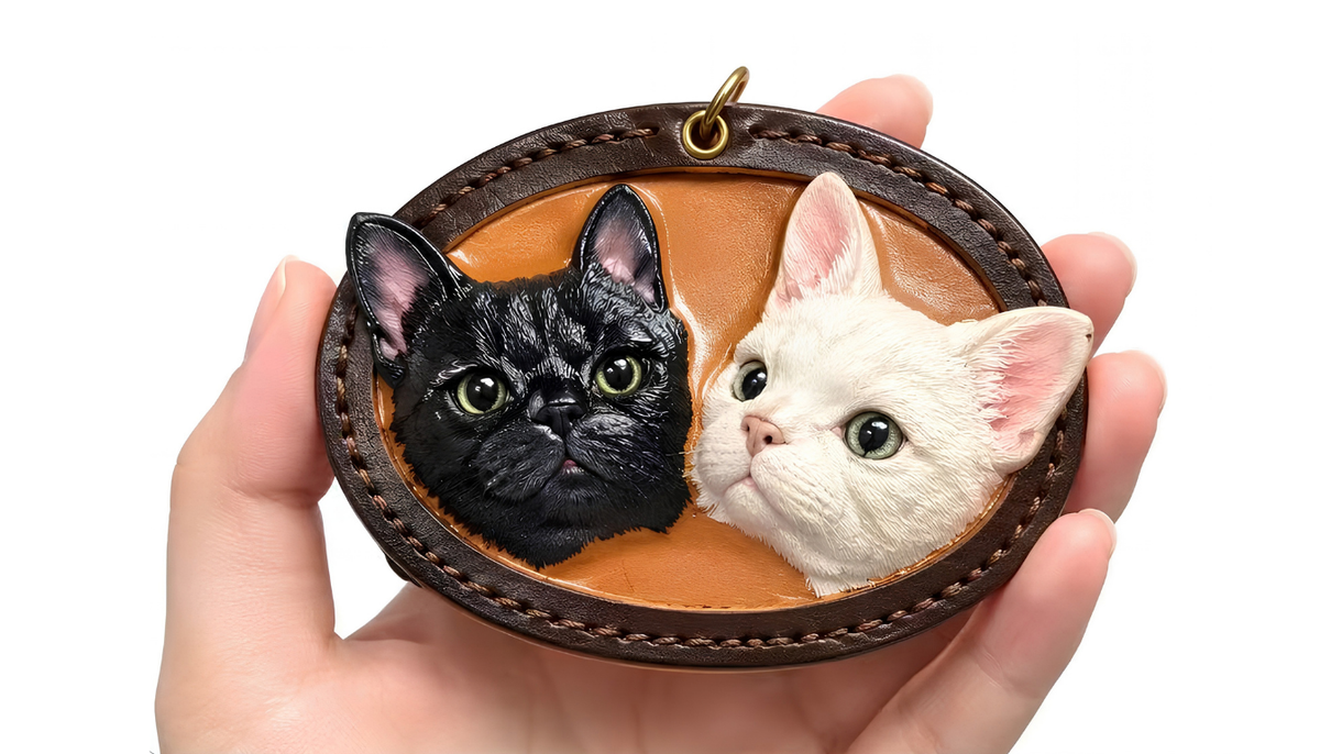Pet relief ornament close-up in hand, two cats on oval brown backing with gold loop