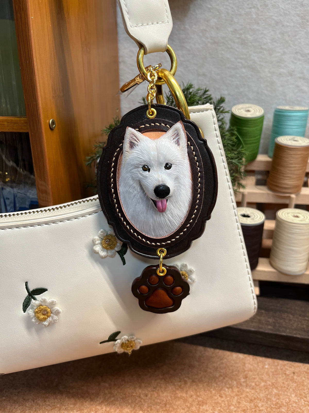 Black oval leather dog charm on a bag, with paw tag and small flower accents