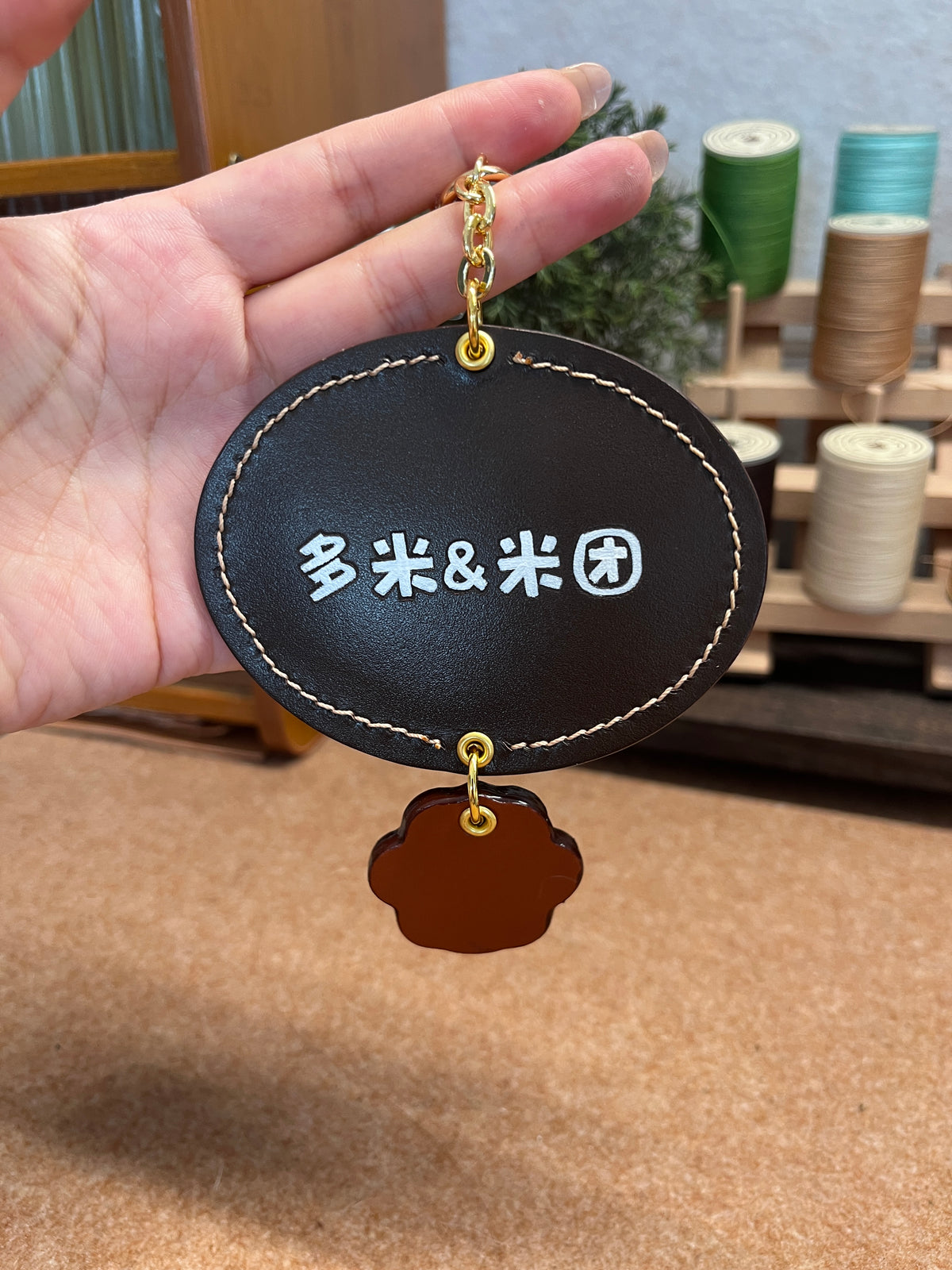 Black oval pet keychain with white characters, gold ring, and small brown charm