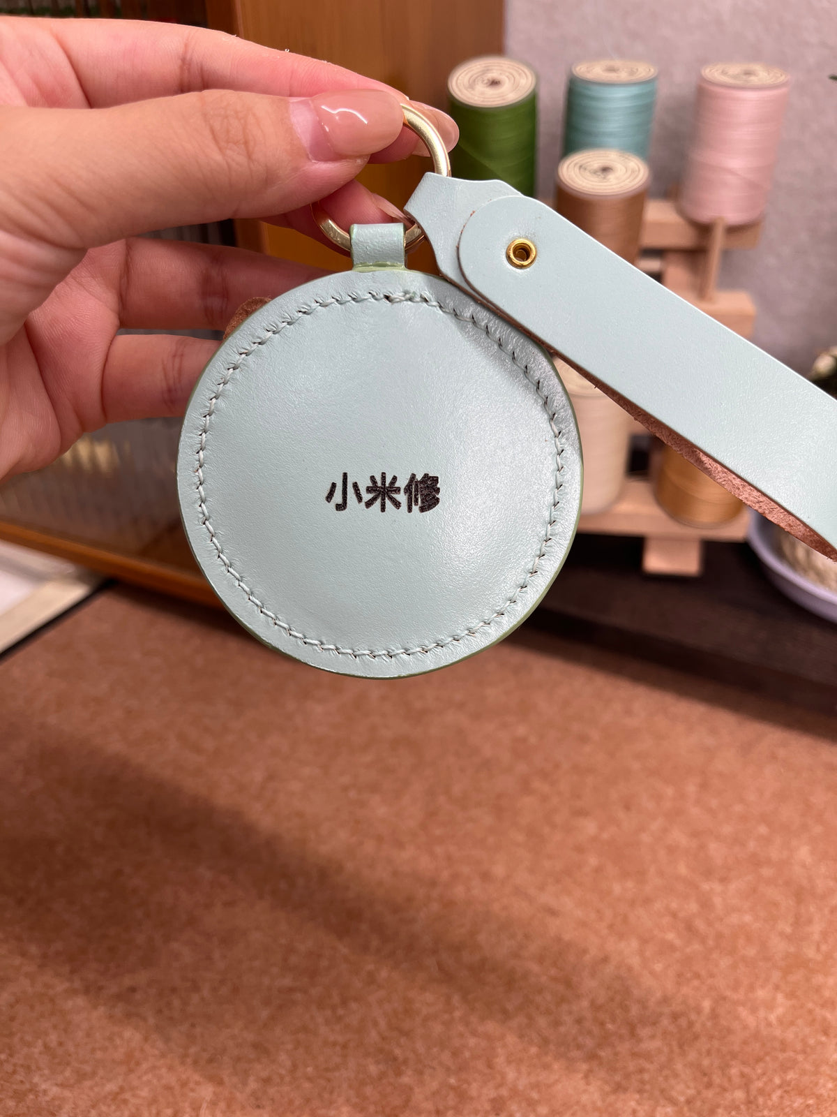 Round light-blue leather keychain with stitched edge and metal key ring clasp