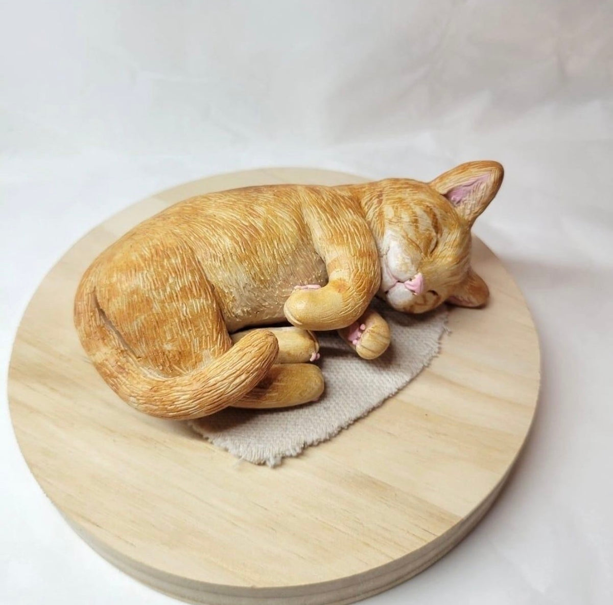 Custom 3D pet figurine of an orange cat curled up on a round wooden base